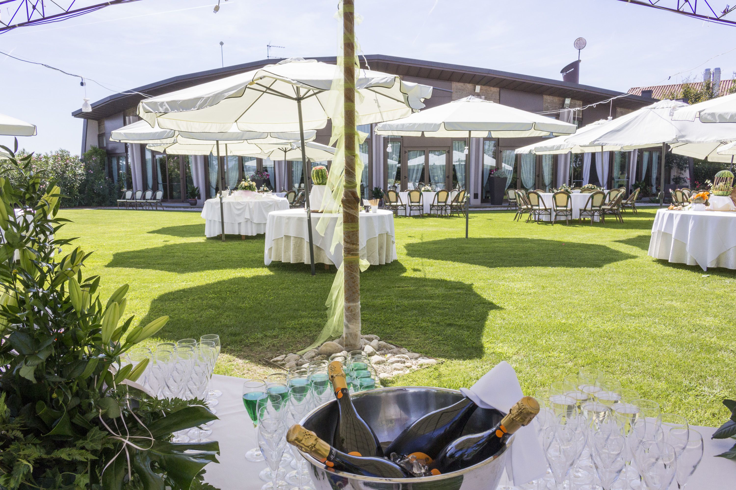 Un espace extérieur aménagé pour les événements, avec des tables rondes, des parasols blancs et un seau à champagne.