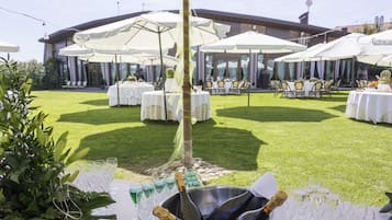 Un espace extérieur aménagé pour les événements, avec des tables rondes, des parasols blancs et un seau à champagne.
