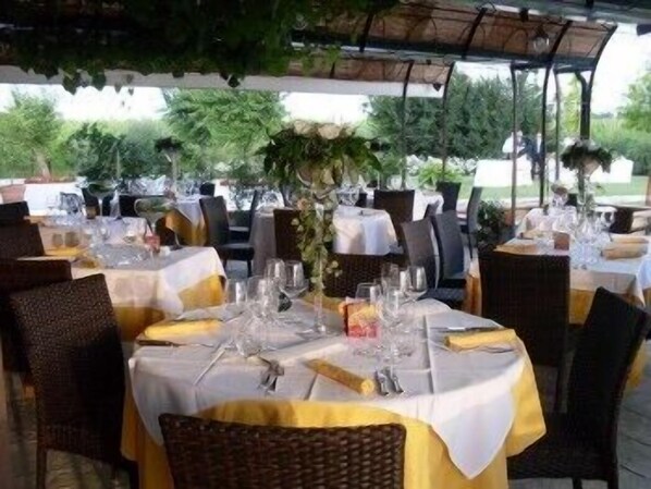 Un área de comedor al aire libre con mesas redondas cubiertas con manteles blancos y servilletas amarillas.