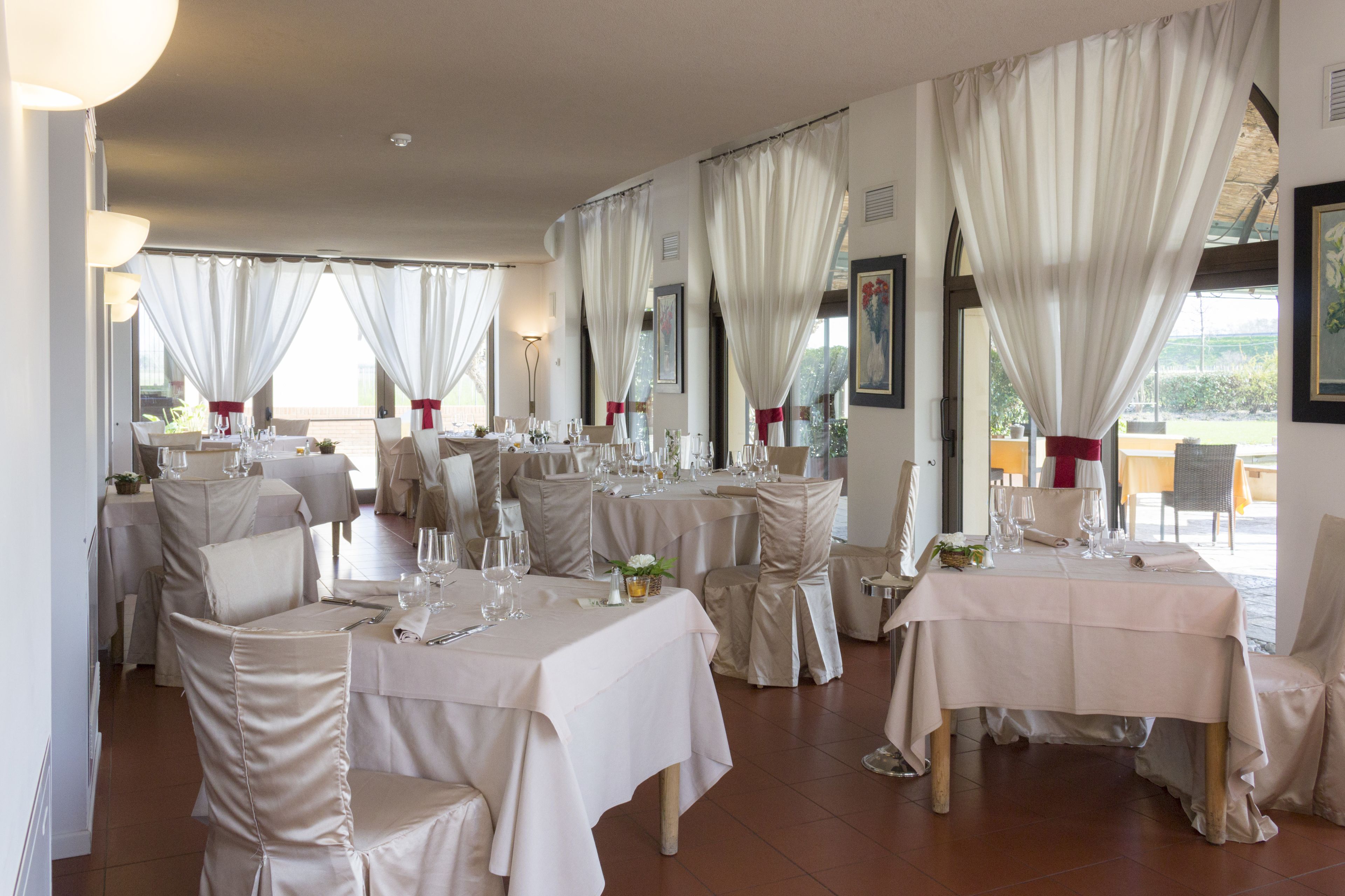 Un restaurante con varias mesas dispuestas para comer, con manteles blancos y sillas adornadas con cintas rojas.