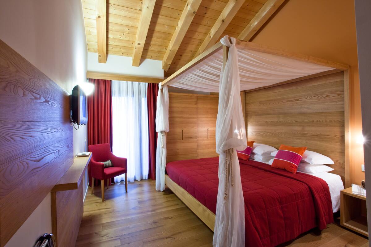 Une chambre avec un plafond en bois, un lit à baldaquin, une chaise rouge et une table de chevet en bois.