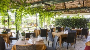 An outdoor restaurant with tables and chairs, covered by a pergola with vines.