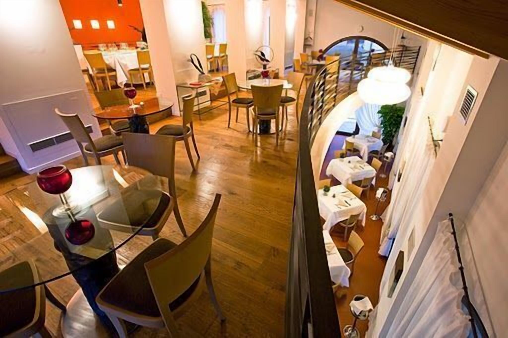 A hotel dining area with multiple tables and chairs, a staircase, and a view of the adjacent room.