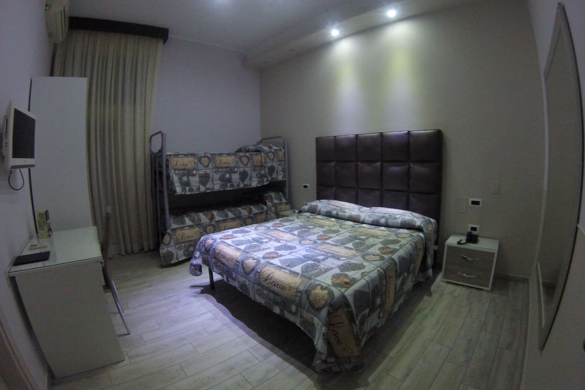 A compact bedroom with a bunk bed, a desk with a computer, and a bedside table with a phone.