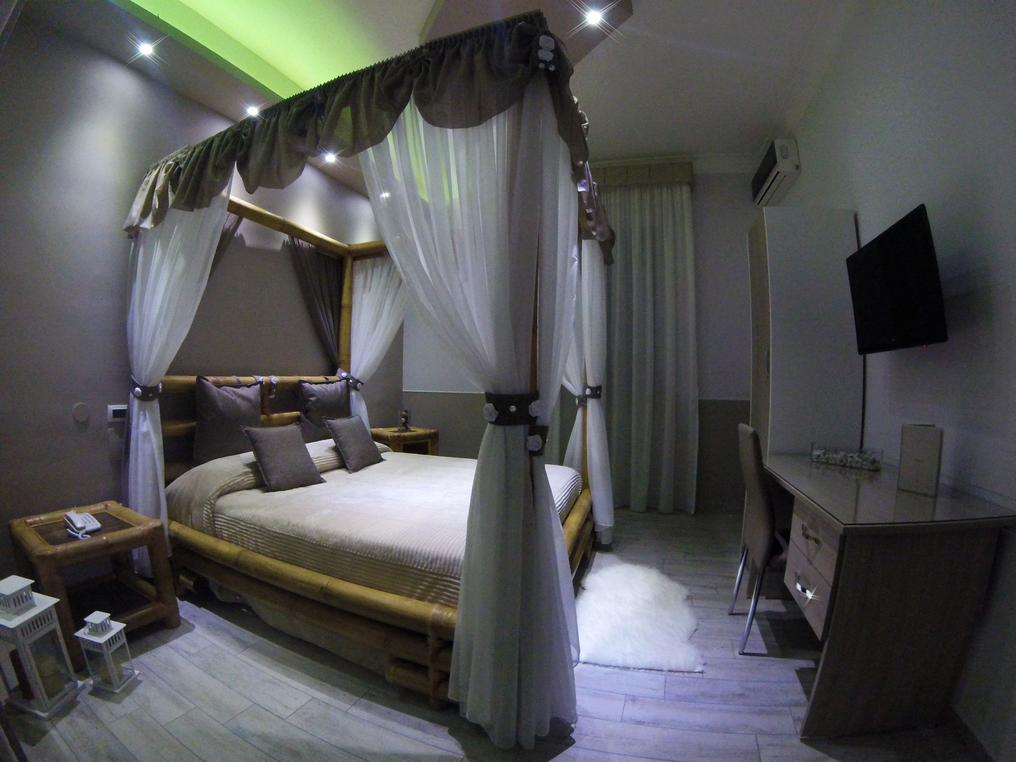 Ein Schlafzimmer mit Himmelbett, Nachttischen, Schreibtisch und Flachbildfernseher.