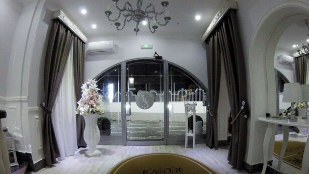 A hotel entrance with a chandelier, a white reception desk, and a large window with a view of the outside.