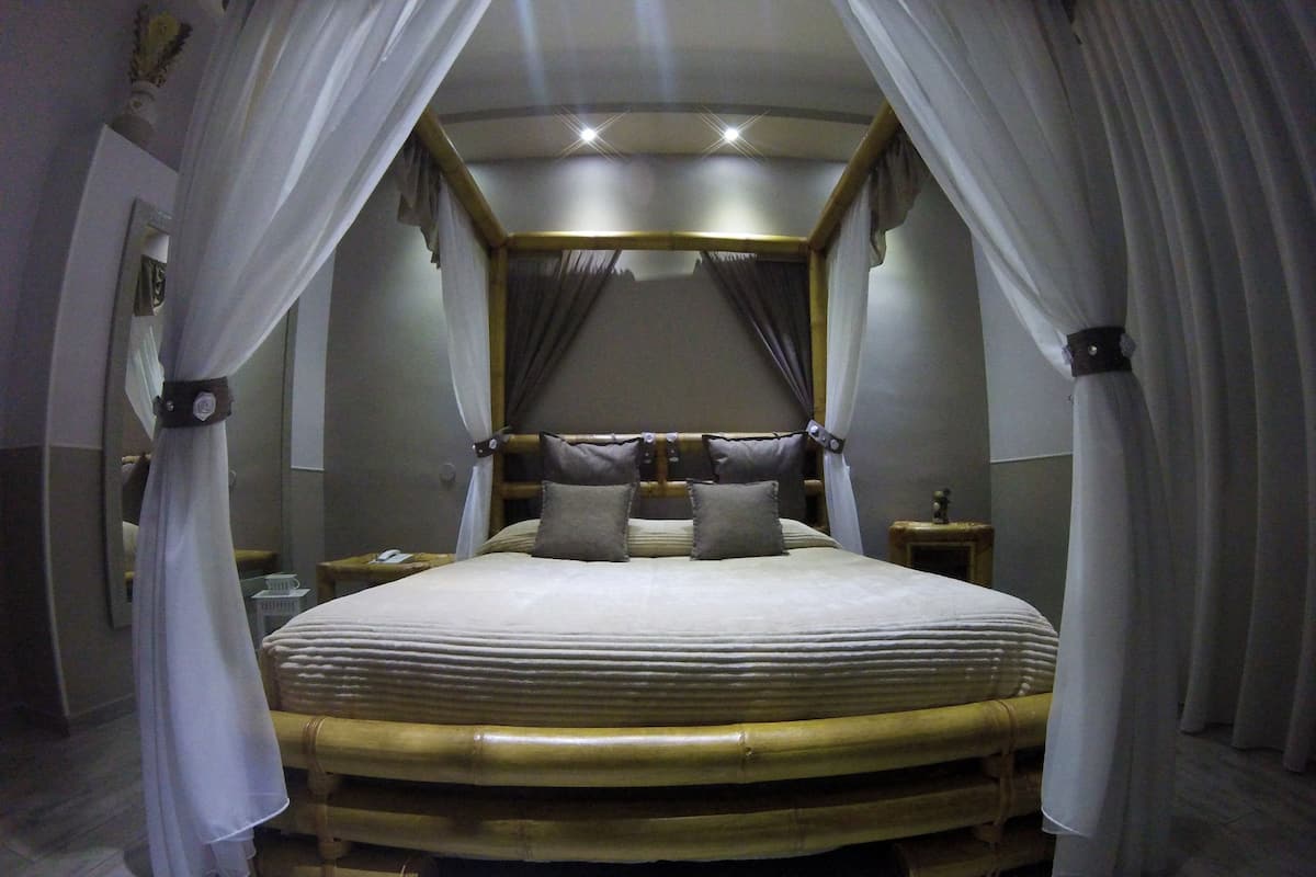 A bed with a headboard, draped curtains, and a nightstand with a lamp.