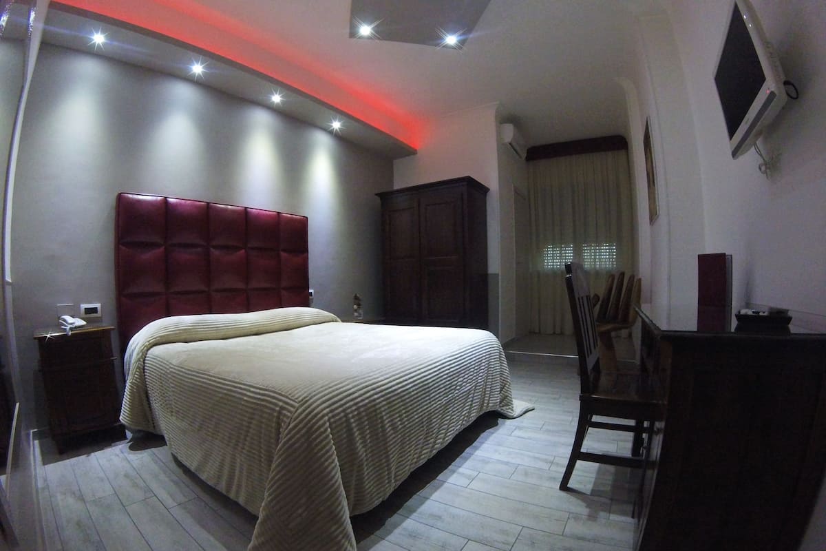 A bedroom with a large bed, a wardrobe, a desk, and a chair.