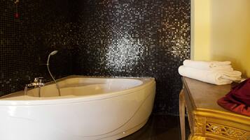 Un baño moderno con una bañera independiente, un tocador con marco dorado y una pared de mosaico oscuro.