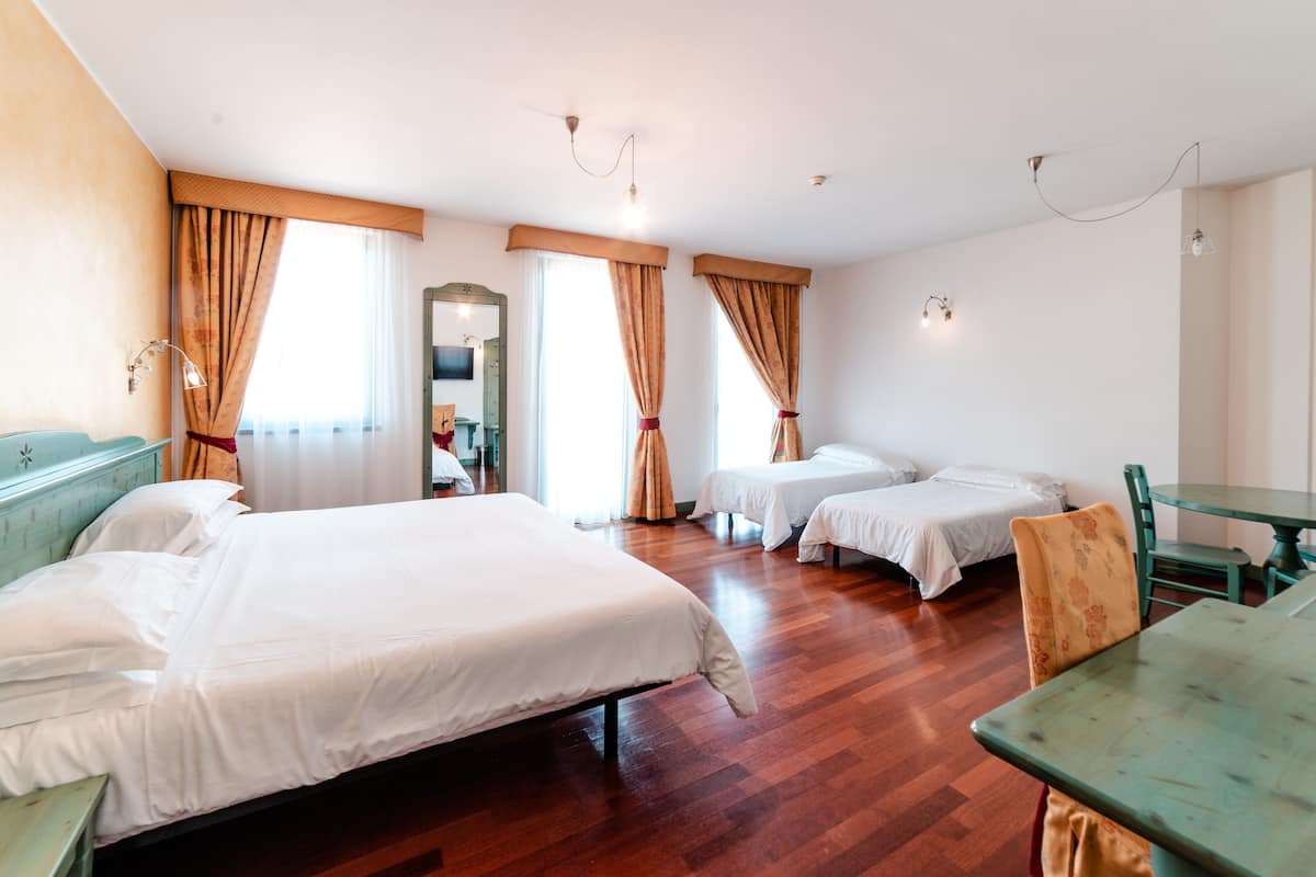 A hotel room with two single beds, a wooden floor, a dining table, and a mirror.