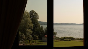 A view through a window of a lake with trees and a small building in the foreground. - Hotel Residence Montelago (Ternate)