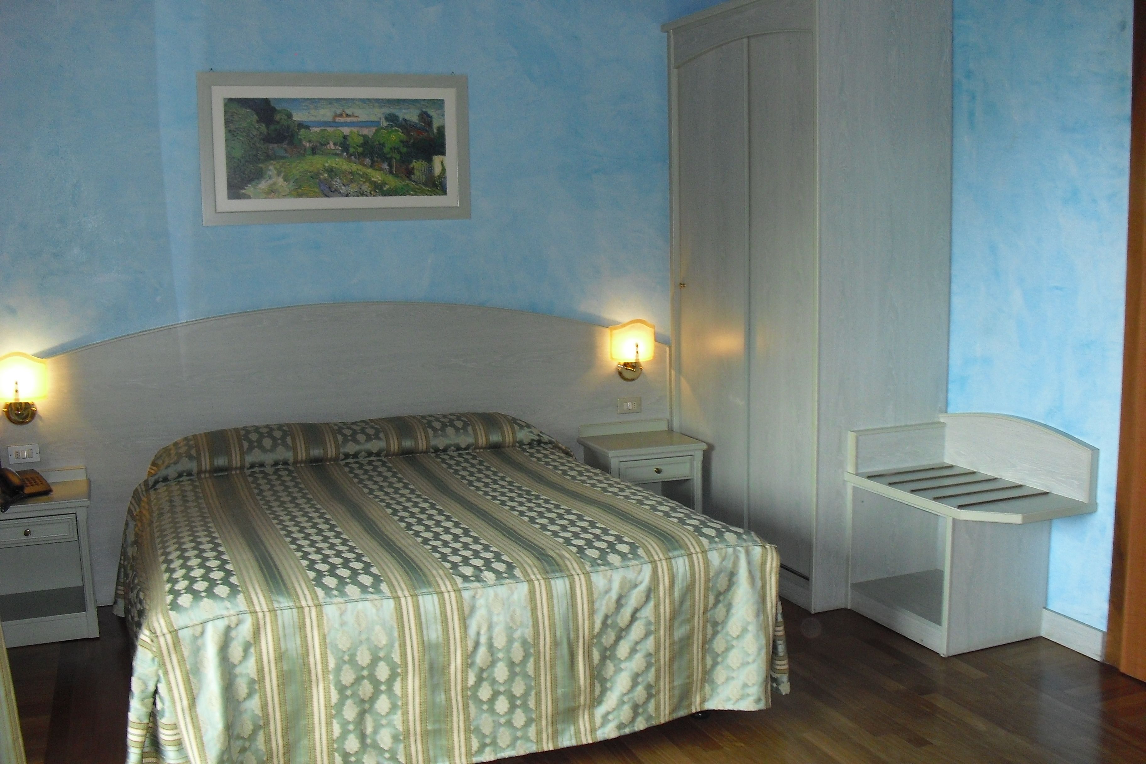 A bedroom with a bed, bedside tables, a nightstand, a wardrobe, and a wall-mounted shelf.