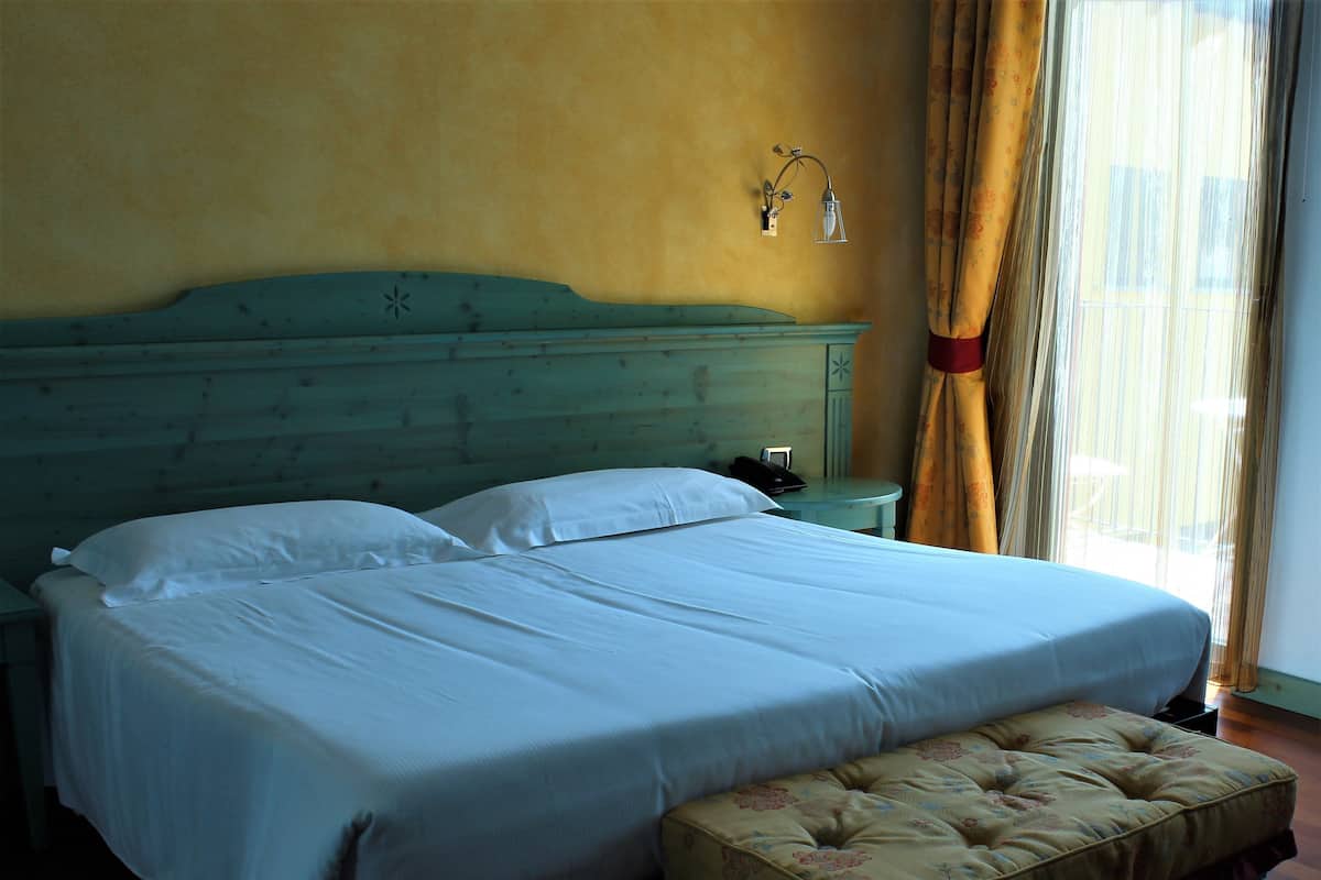 A bed with white linens, a wooden headboard, and a bedside table with a lamp.