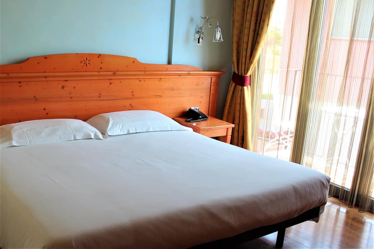 A neatly made bed with white linens, a wooden headboard, and a bedside table with a lamp and a phone.