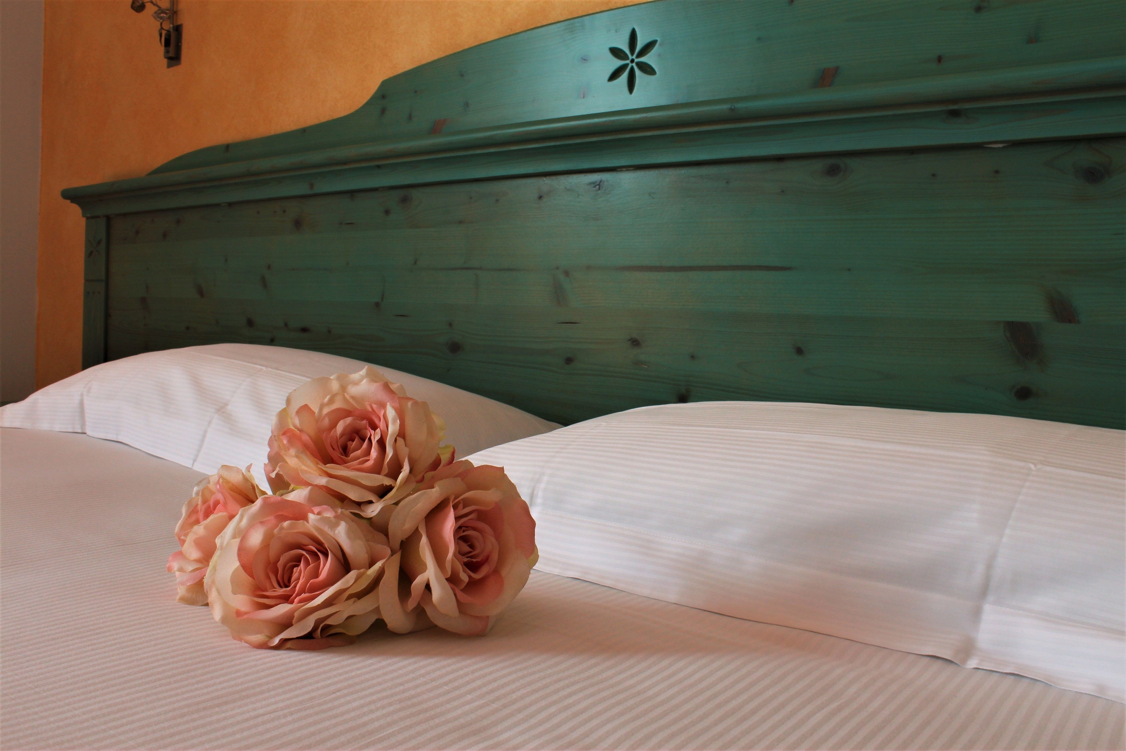 A bed with white linens and a bouquet of pink roses.