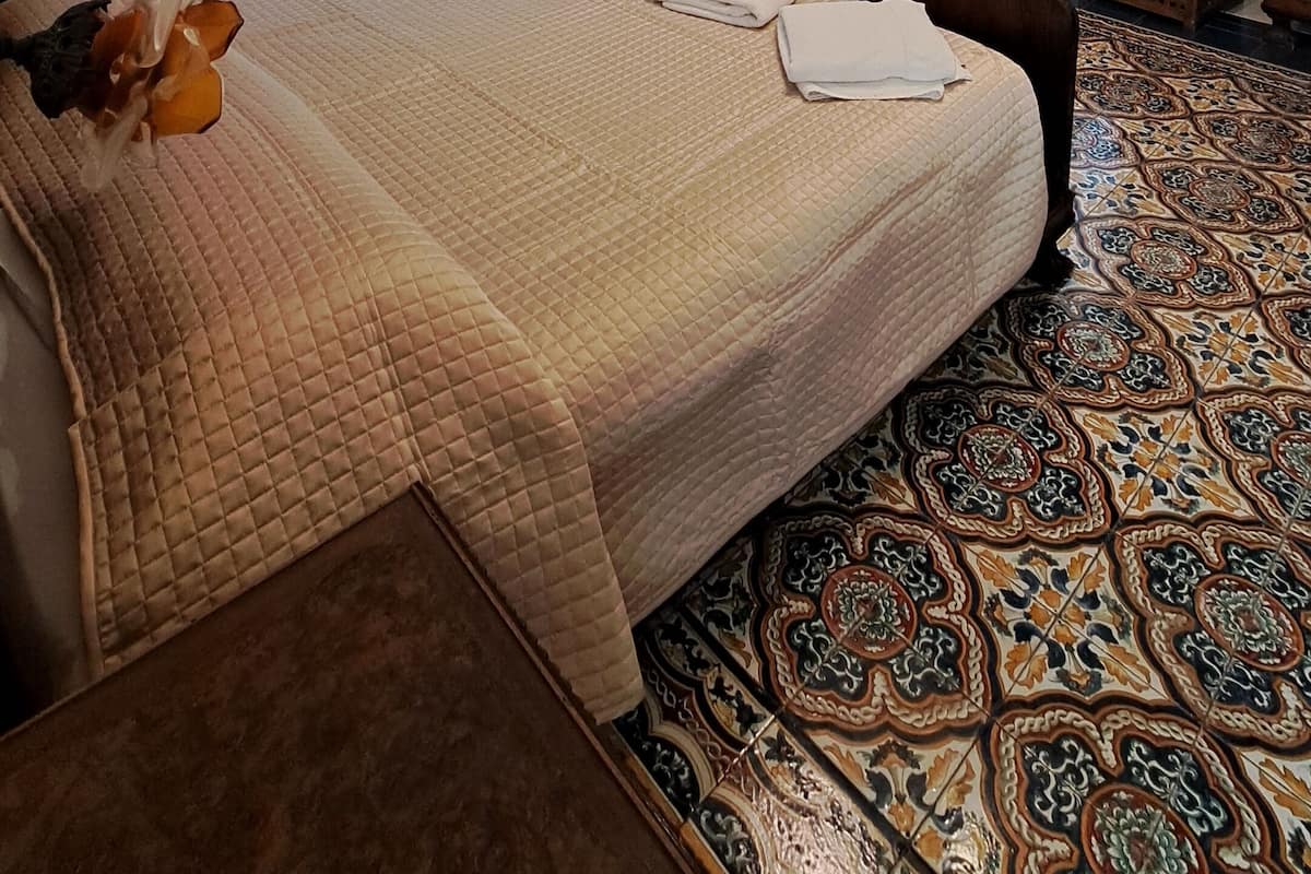 A hotel room with a large bed, a wooden wardrobe, a mirror, and patterned floor tiles.