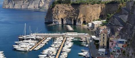 A marina with boats docked, a rocky coastline, and buildings on the cliff.