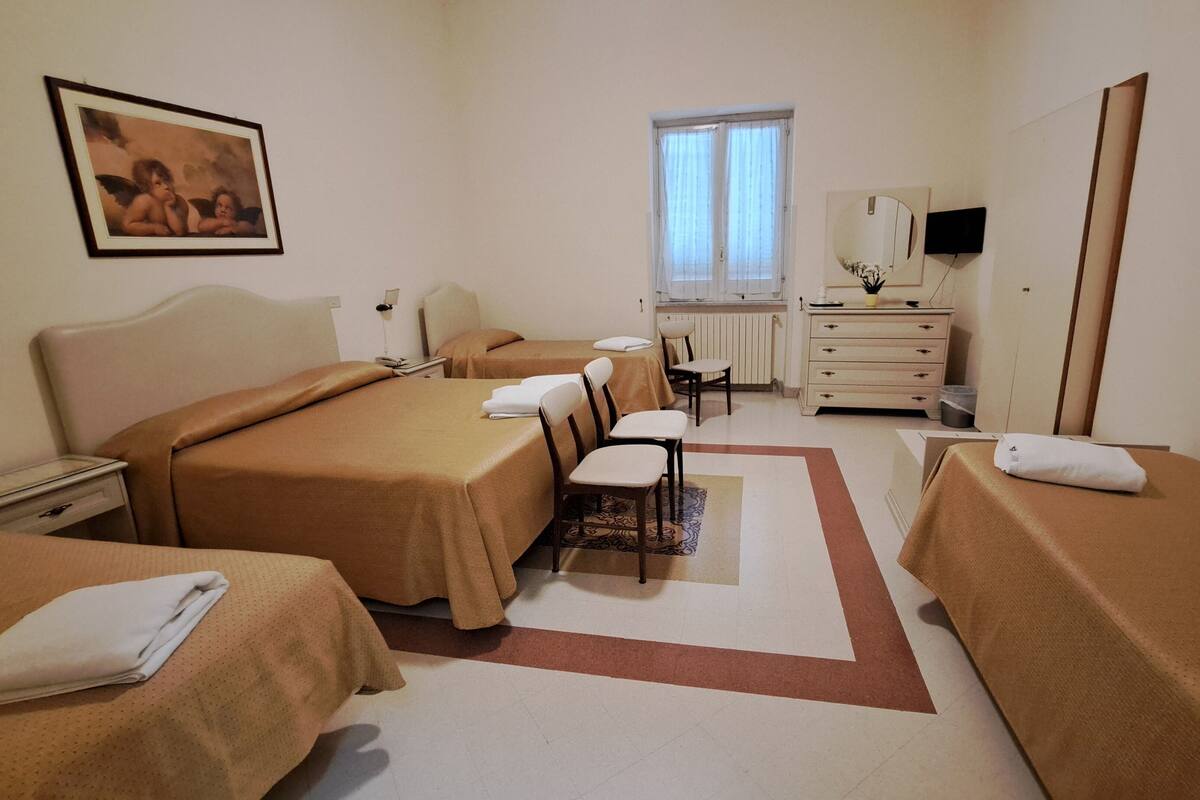 A hotel room with two beds, a desk, a chair, a dresser, a mirror, and a window.