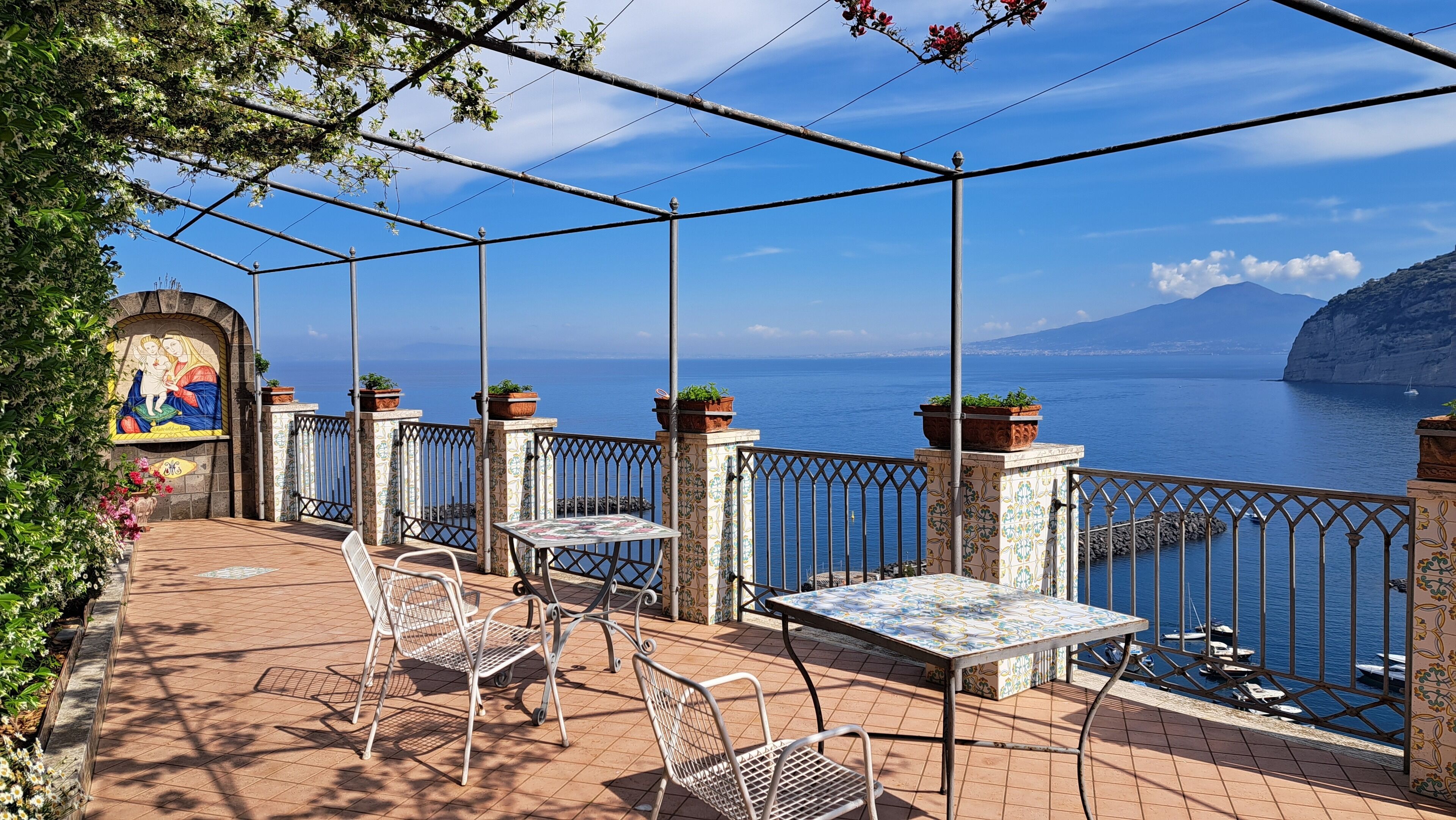 A terrace with outdoor seating, a mural, and a view of the sea.