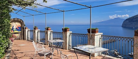 A terrace with outdoor seating, a mural, and a view of the sea.