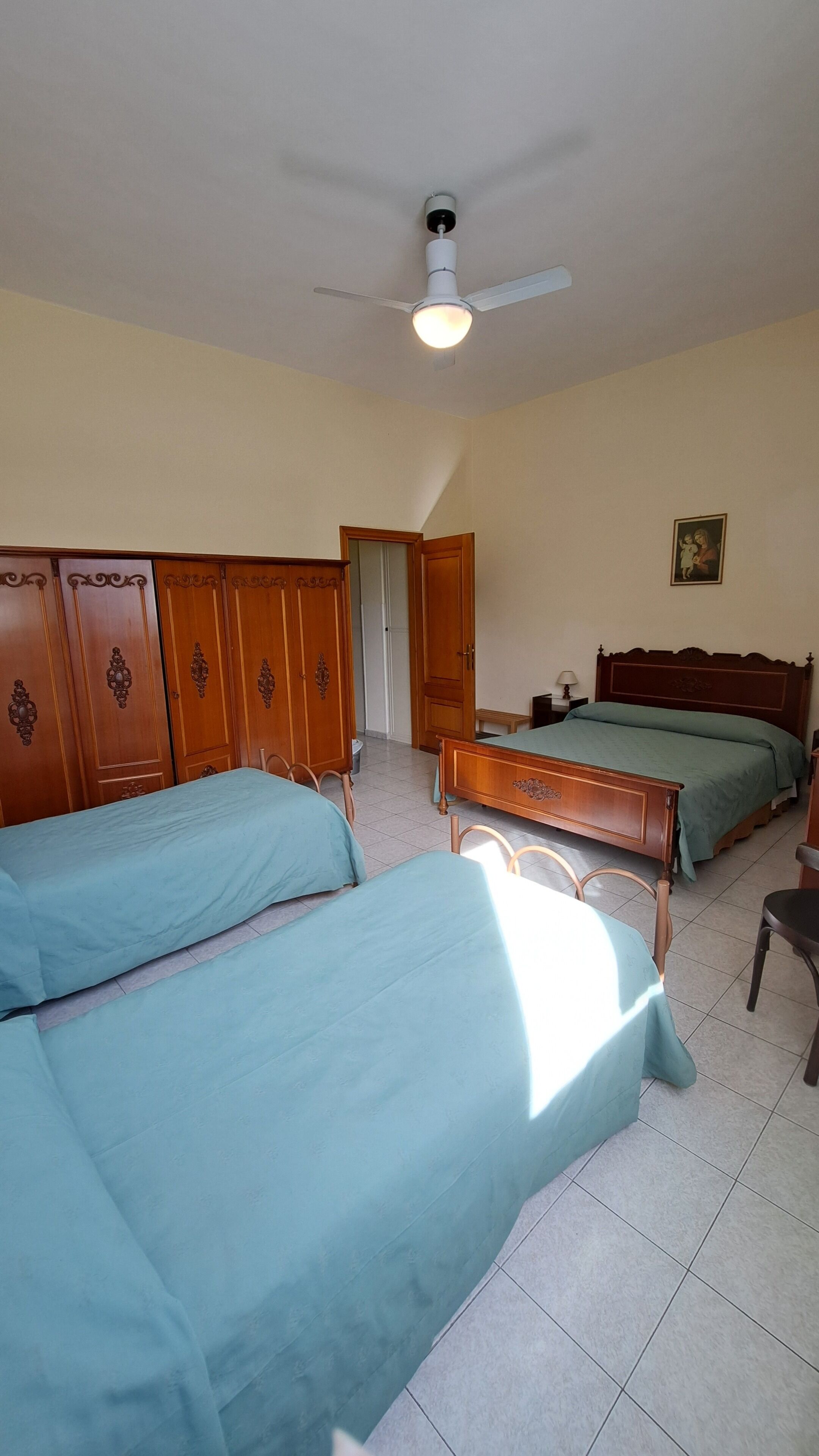 Une chambre avec deux lits simples, une armoire en bois, un ventilateur de plafond et une table de chevet avec une lampe.