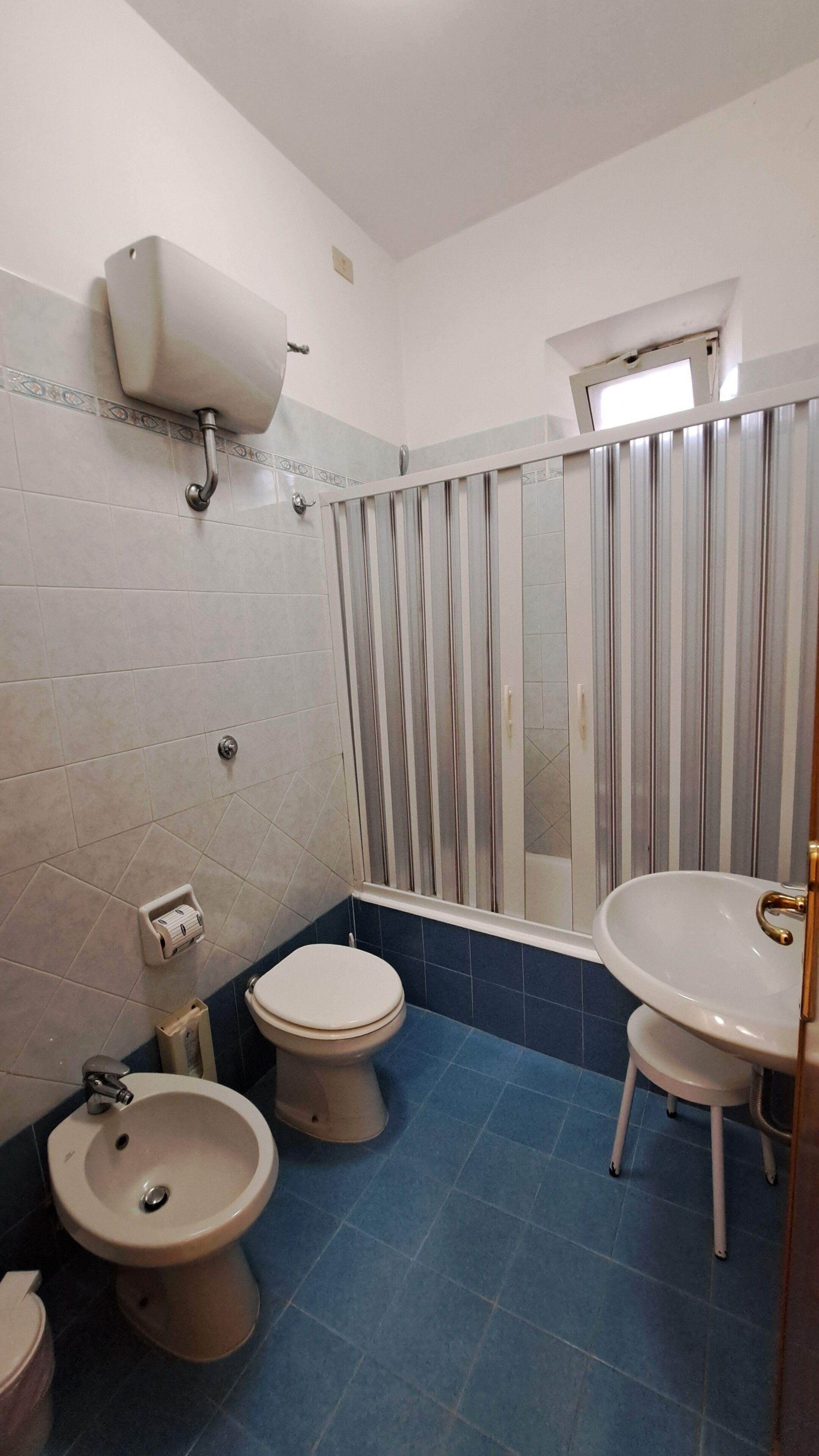 Et badeværelse med to toiletter, et pissoir, en håndvask og en bruser med bruseforhæng.
