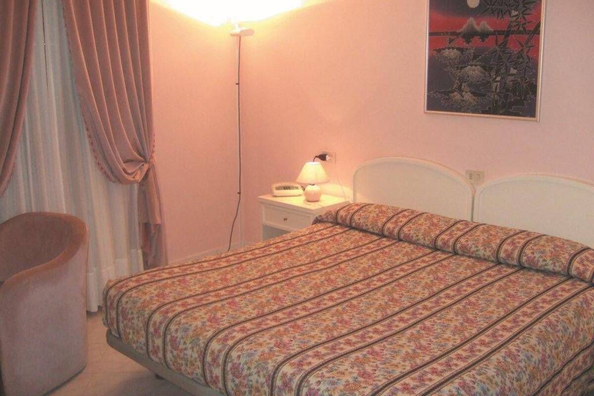 A bedroom with a bed, a nightstand, a lamp, a chair, and a painting on the wall.