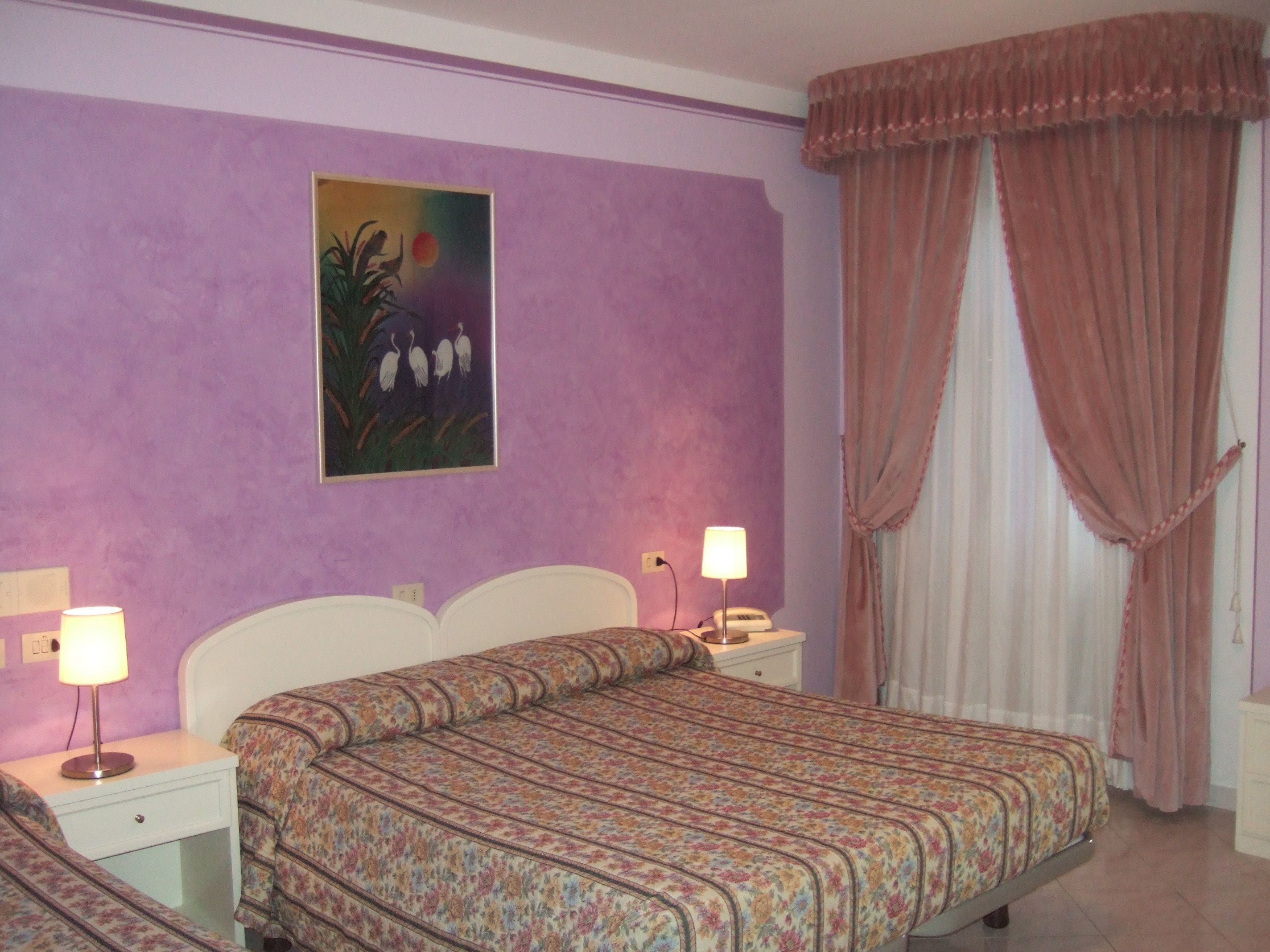 A bedroom with a bed, nightstands, lamps, a painting, and curtains.