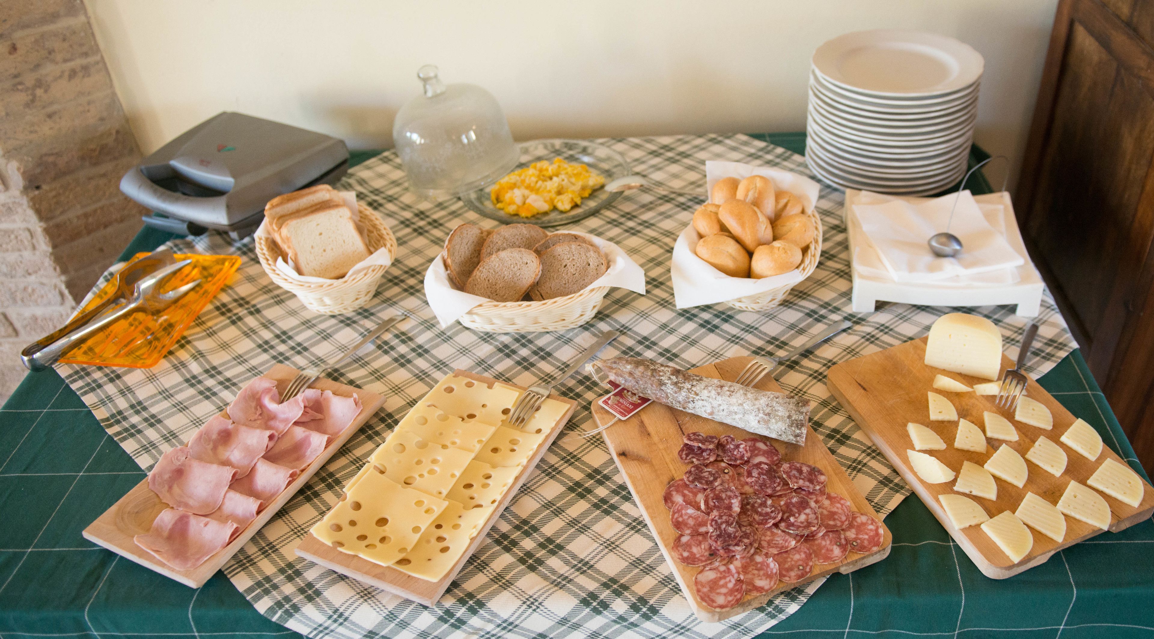 Una mesa con diversos alimentos, como pan, queso y embutidos, sobre un mantel a cuadros.