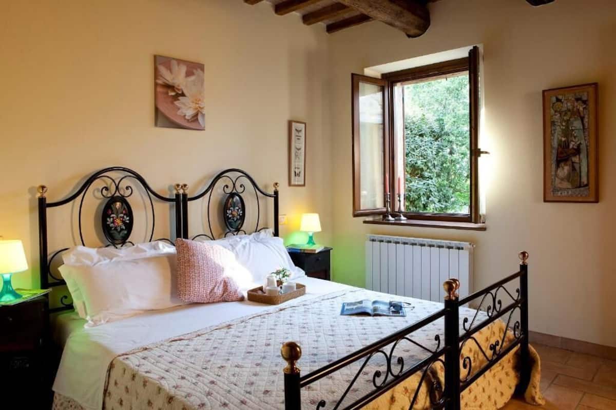 A bedroom with a bed, two bedside tables, a window, and artwork on the walls.