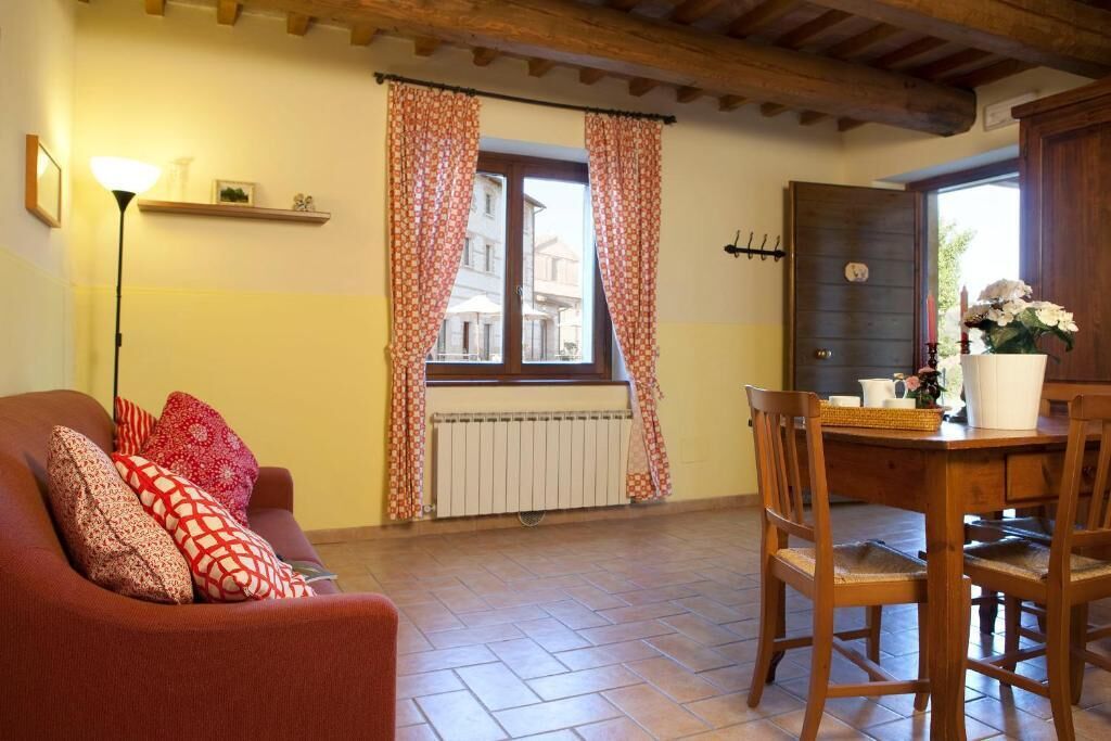 A cozy living room with a sofa, a dining table with chairs, a radiator, and a window with curtains.