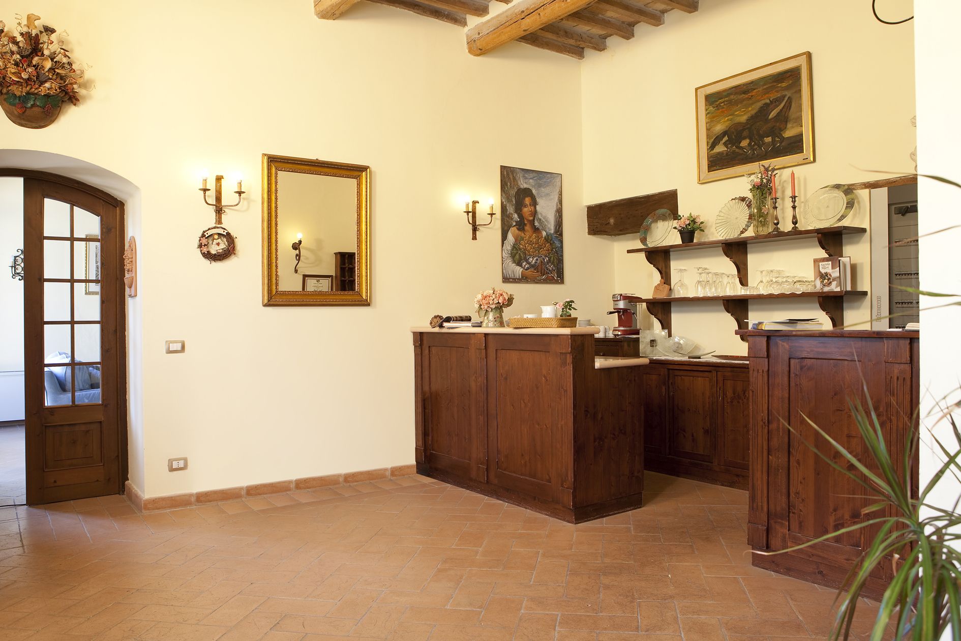 Una habitación con un banco de madera, un espejo, un cuadro y estantes con cristalería.