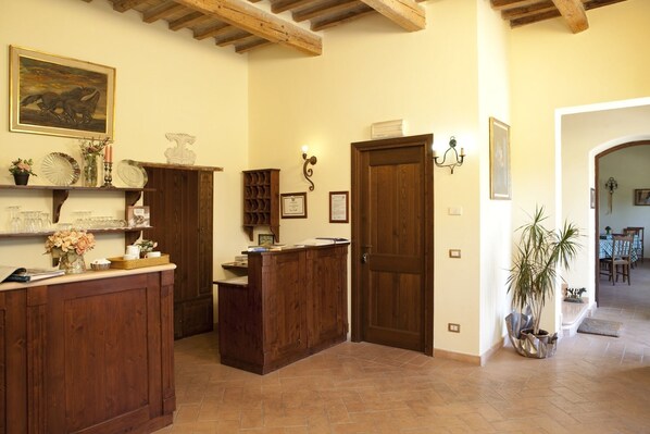 A reception area with wooden furniture, a desk, and a door. There are shelves with decorative items and a plant. - Country House Parco Ducale (Urbania)
