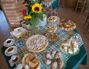 A table with various pastries and desserts, including a large pie and several smaller baked goods, arranged on a checkered tablecloth. - Country House Parco Ducale (Urbania)