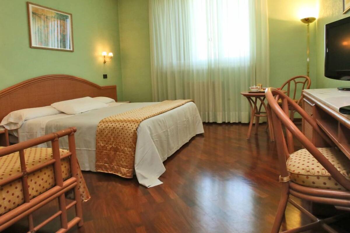 A hotel room with a bed, a desk, a chair, and a television.