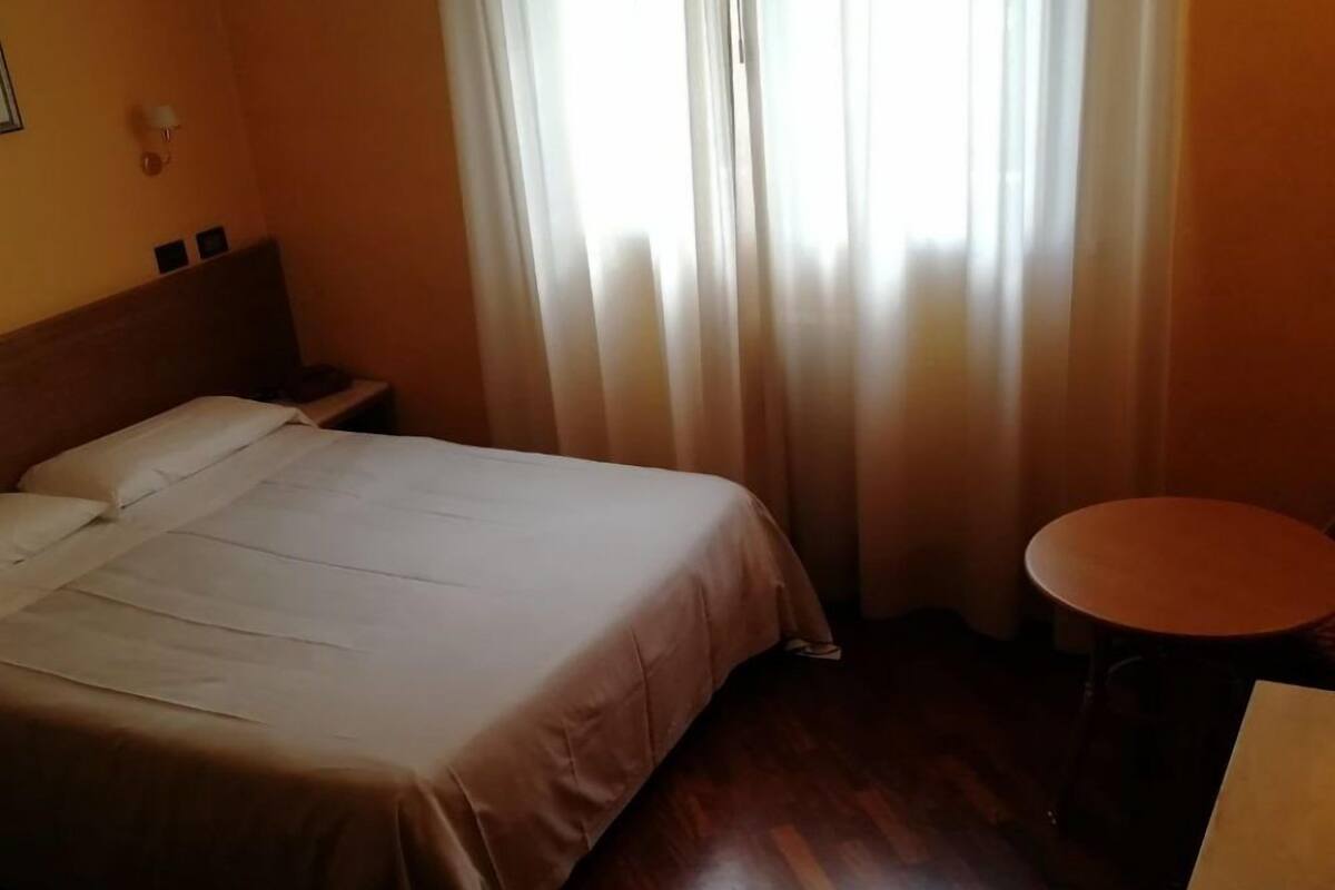 A hotel room with a bed, a small table, and a chair.