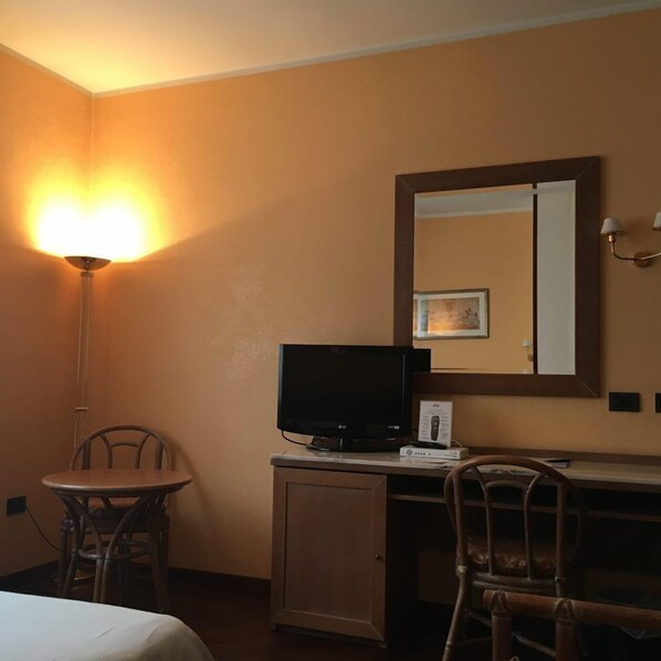Una habitación de hotel con un escritorio, televisión, lámpara y una silla.