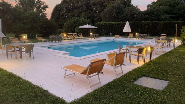Una piscina con lettini e tavoli, immersa nel verde e alberi.