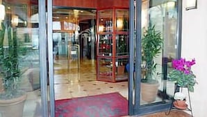 L'ingresso di un hotel con una porta in vetro, una moquette rossa e piante in vaso.
