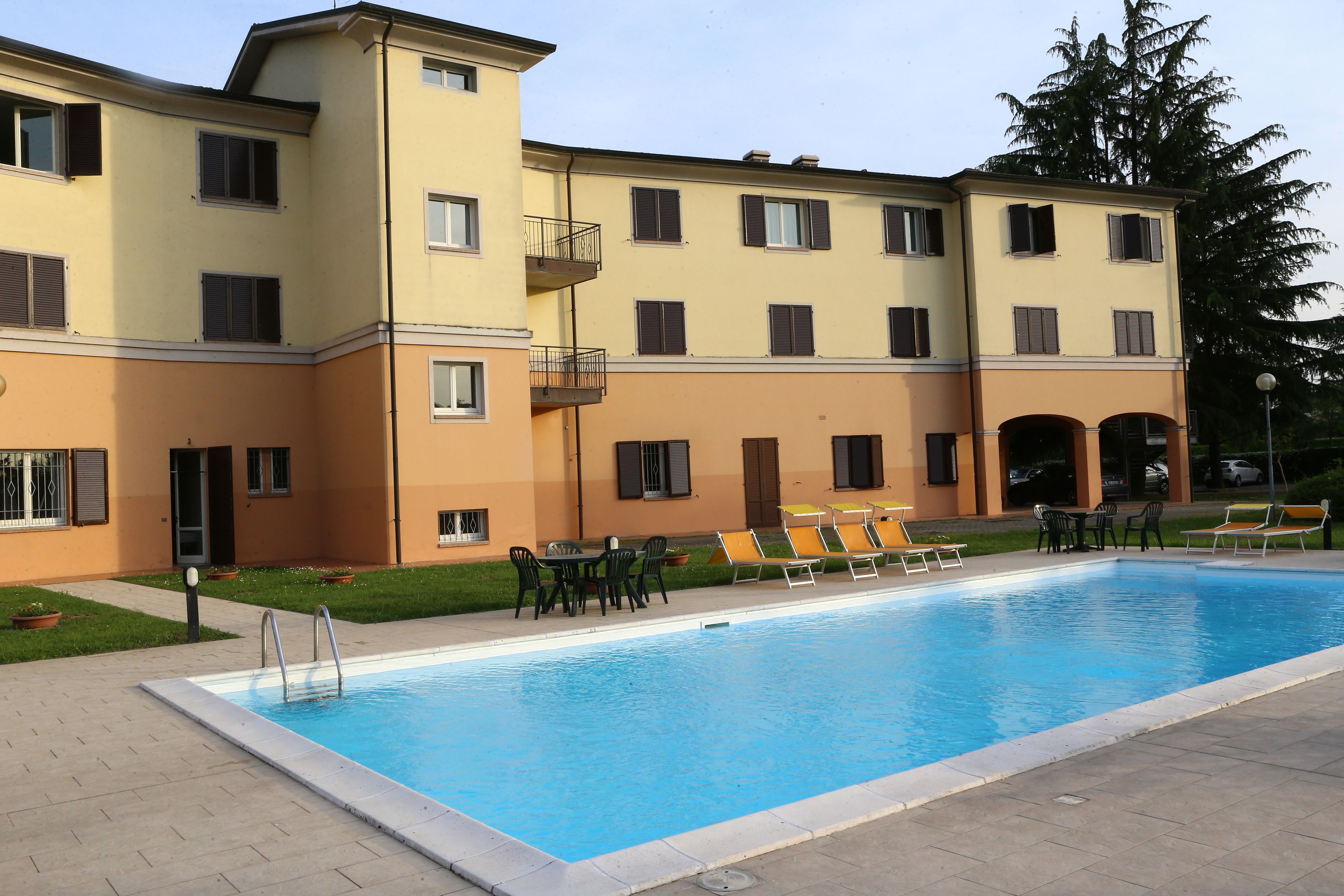 A swimming pool with lounge chairs and a table, surrounded by a building with balconies and windows.