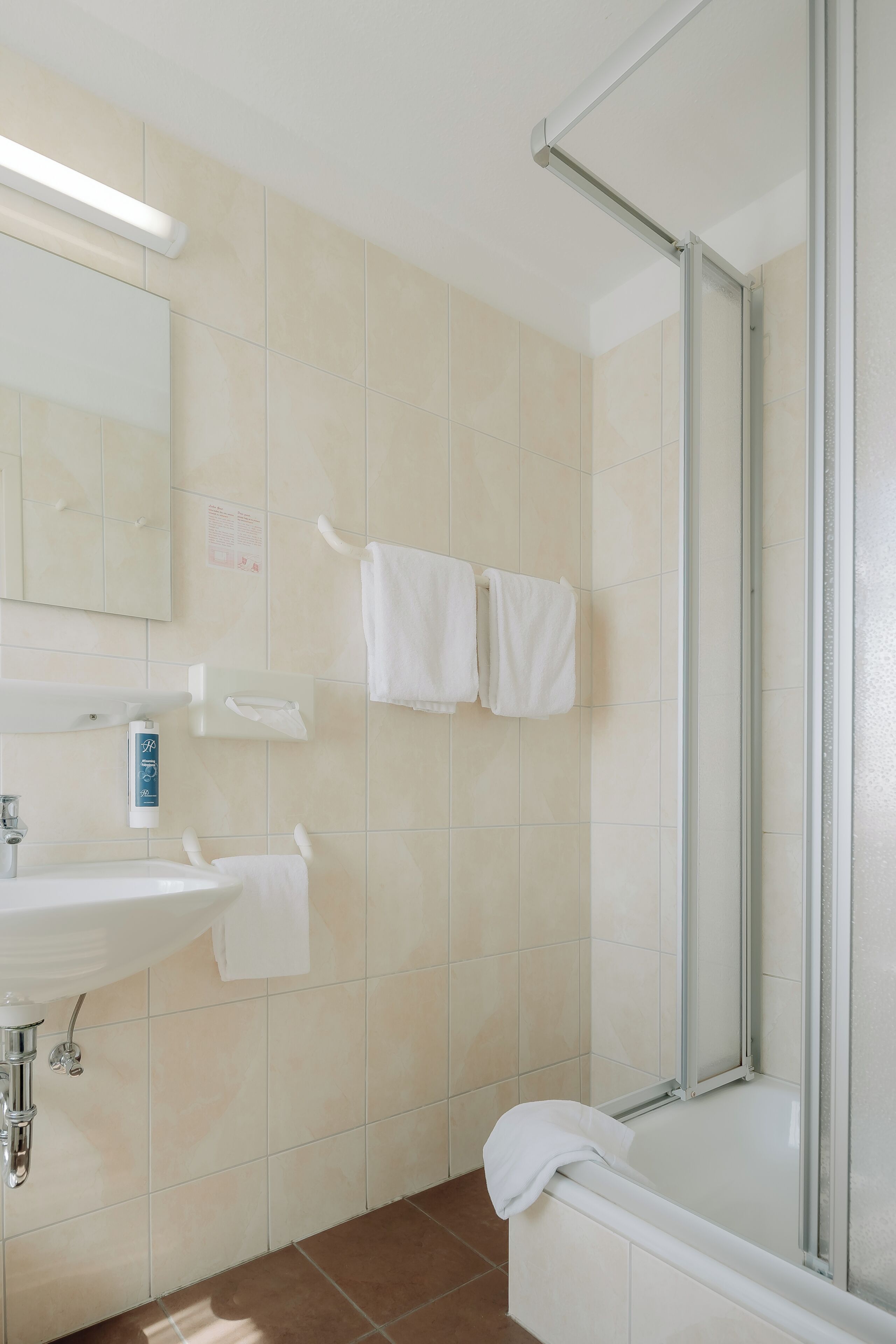 Un baño con lavamanos, espejo, toallero y cabina de ducha.