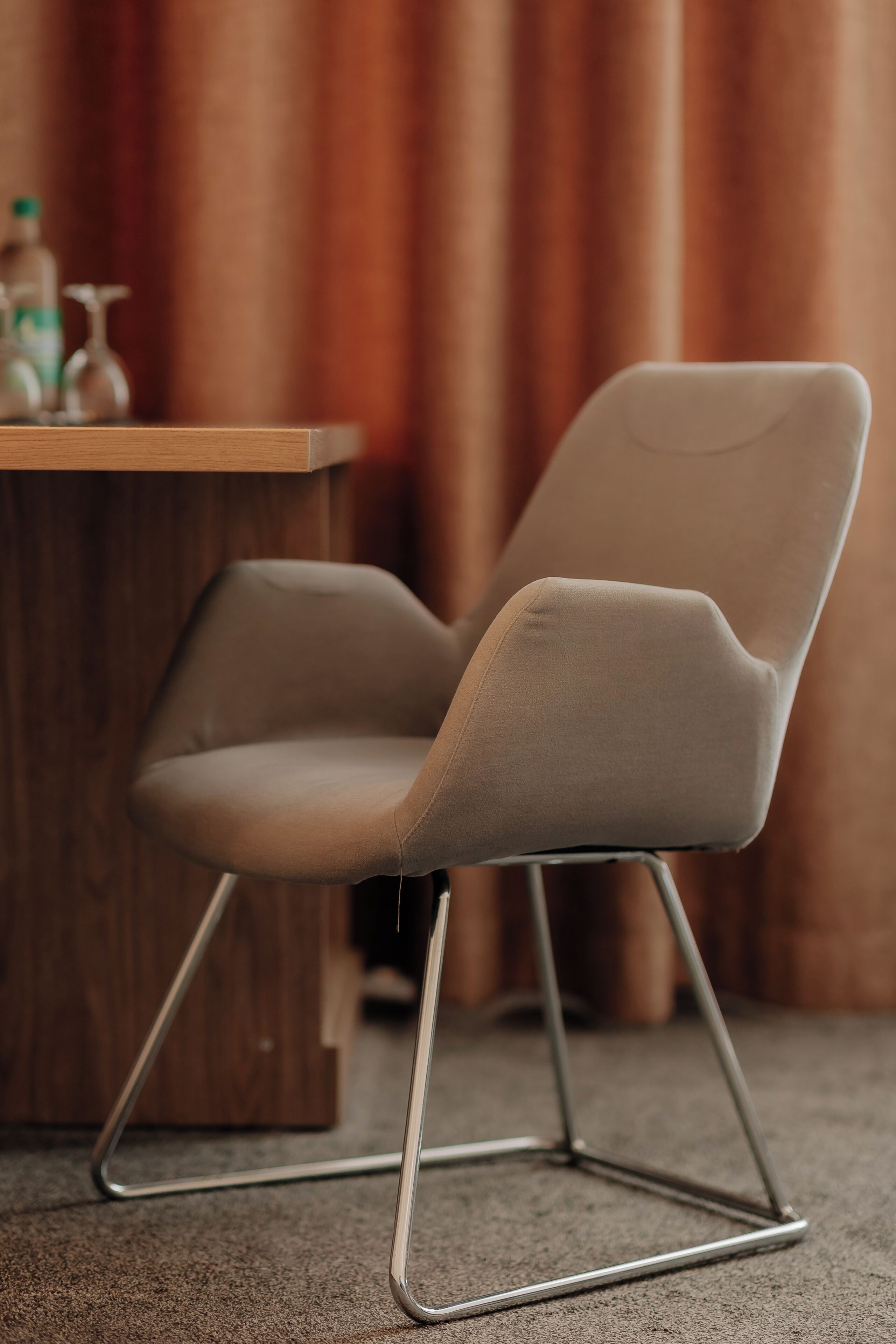 A chair with a unique design, a wooden table, and a curtain in the background.