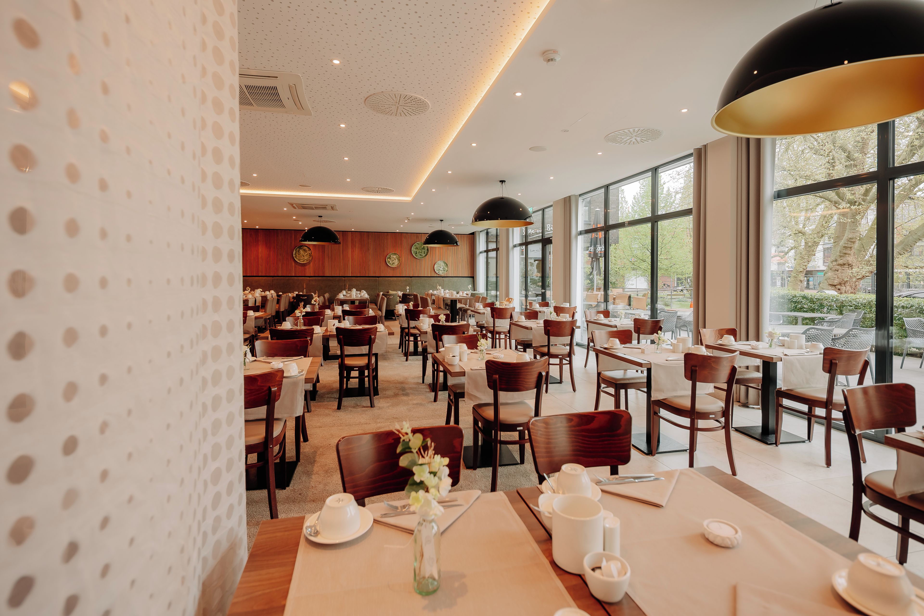 A spacious restaurant with multiple dining areas, large windows, and modern lighting fixtures.