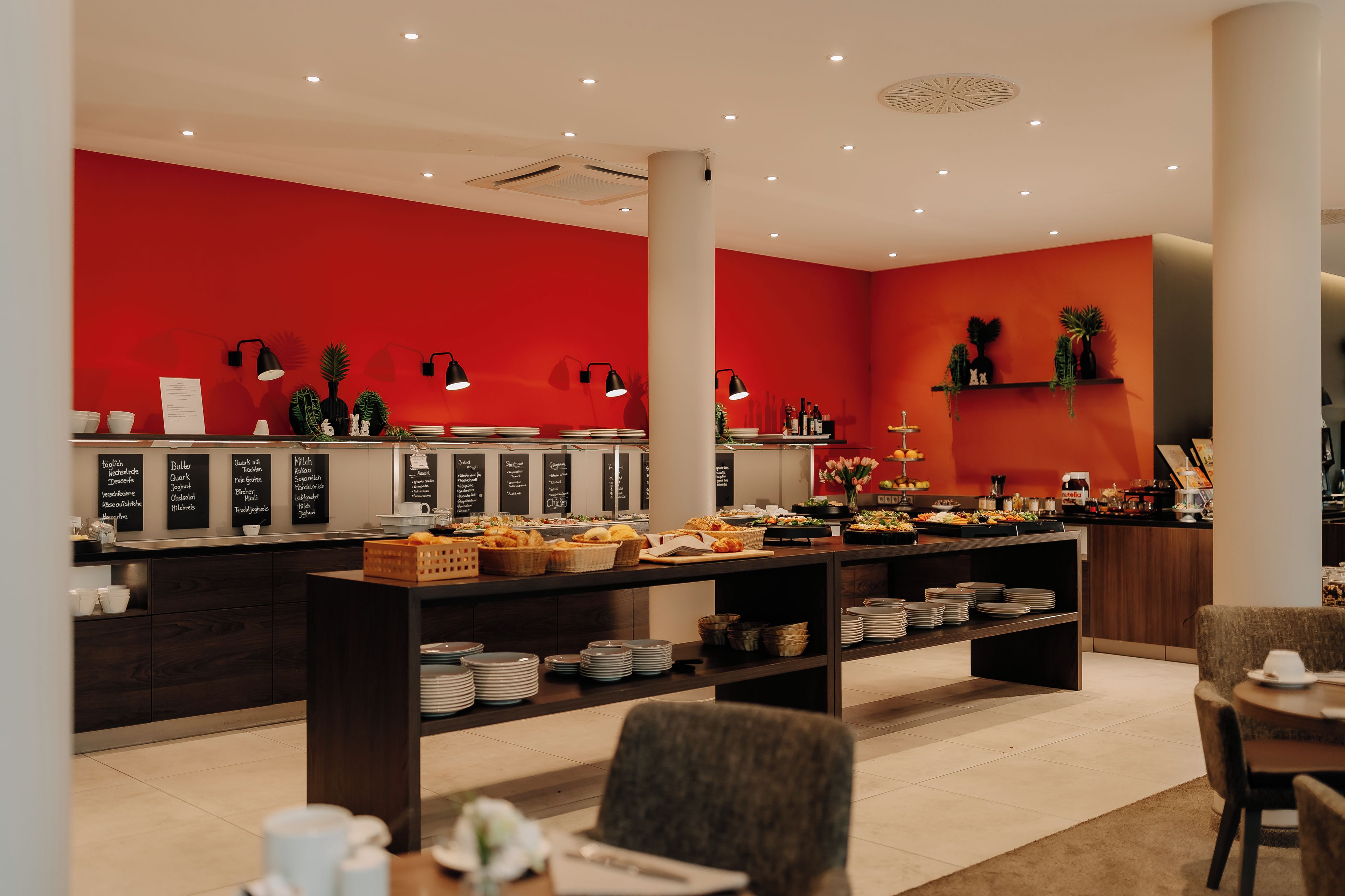 Un'area buffet con parete rossa, diverse postazioni gastronomiche e un'ampia scelta di piatti esposti su tavoli.