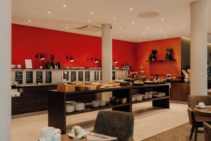 A buffet area with a red wall, multiple food stations, and a variety of dishes displayed on tables. - Parkhotel Lingen by Hackmann (Lingen)