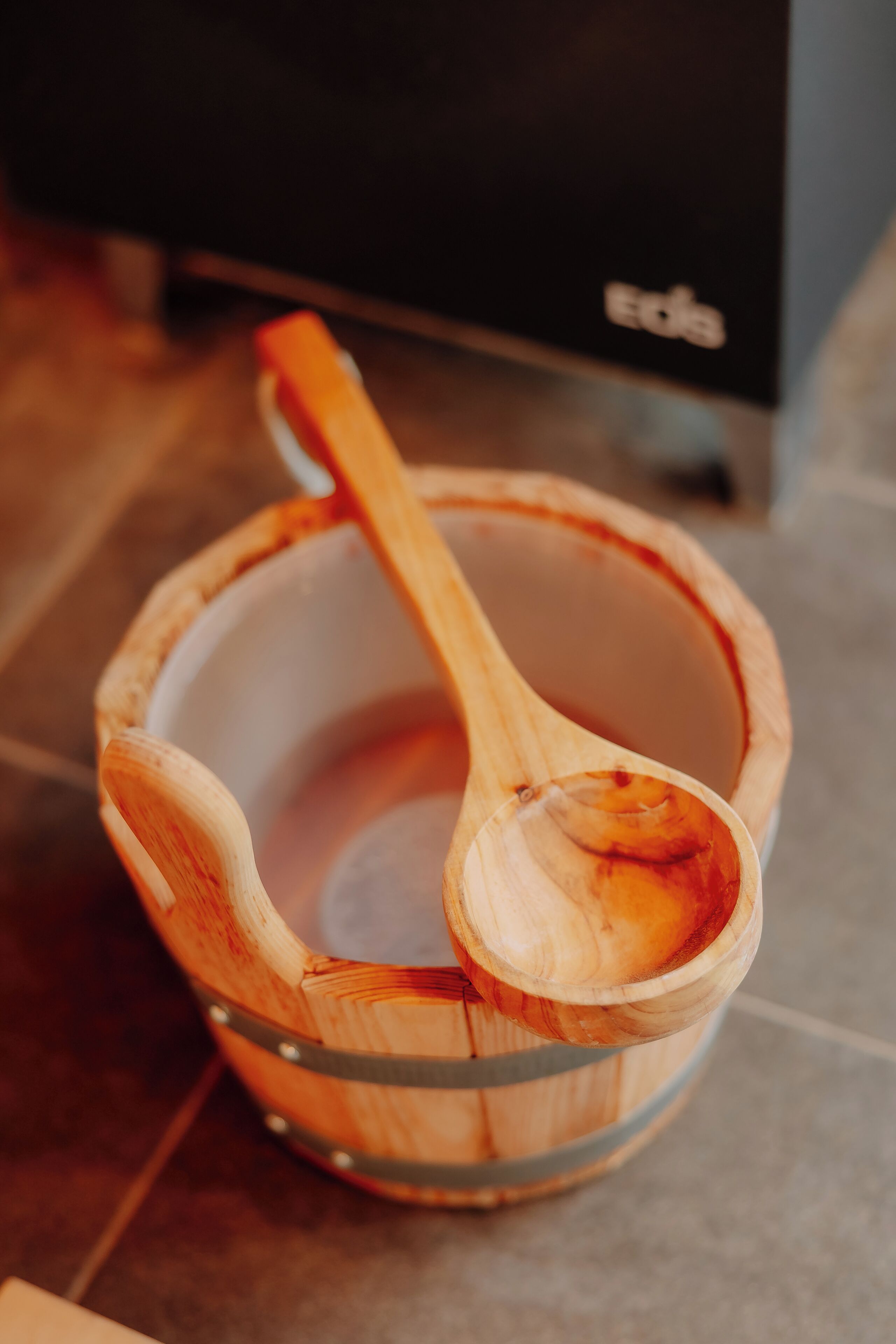 Un tazón de madera con una cuchara en su interior, sobre un piso de baldosas.
