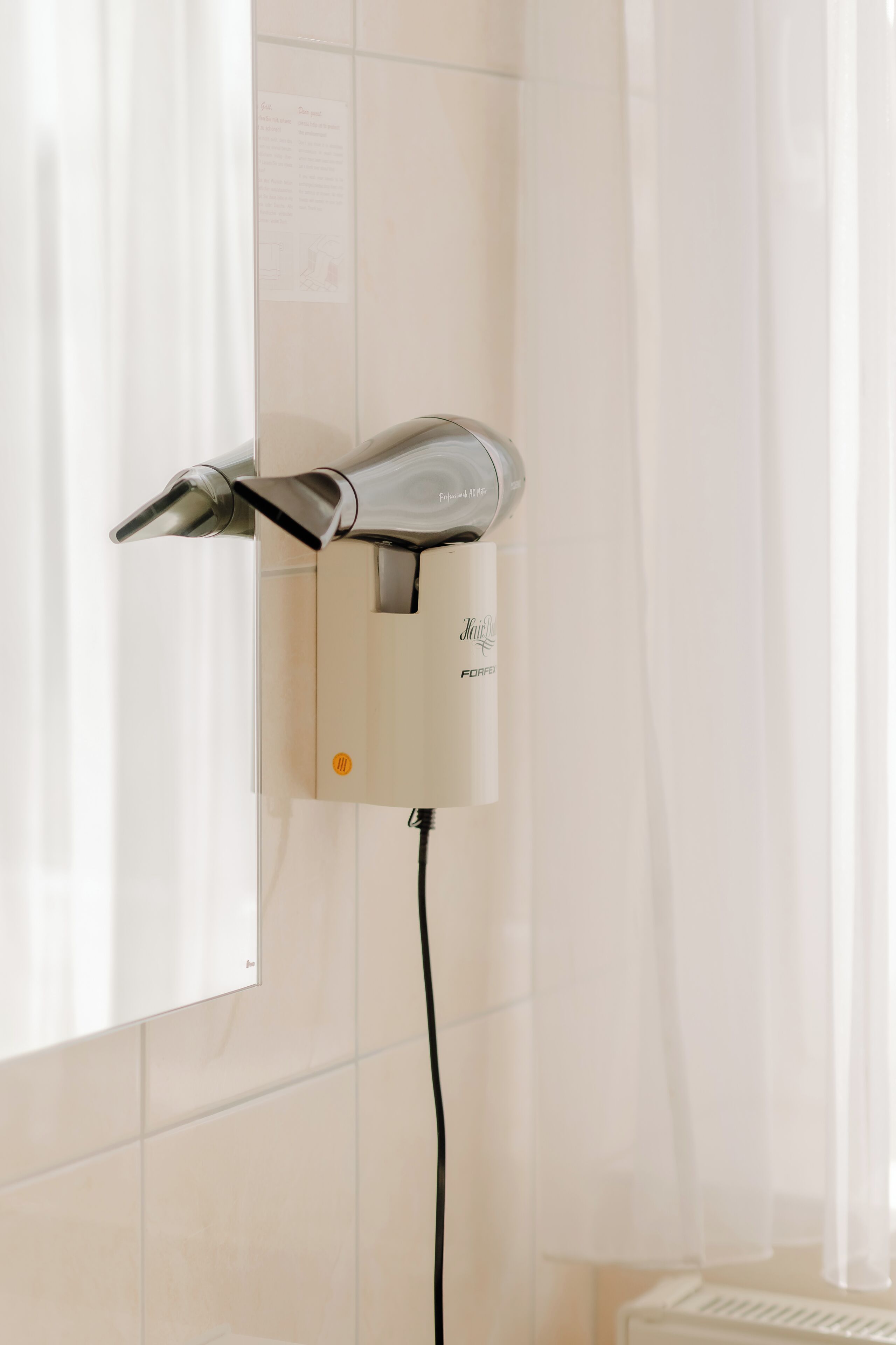 A wall-mounted hairdryer with a control panel, a power cord, and a radiator below.