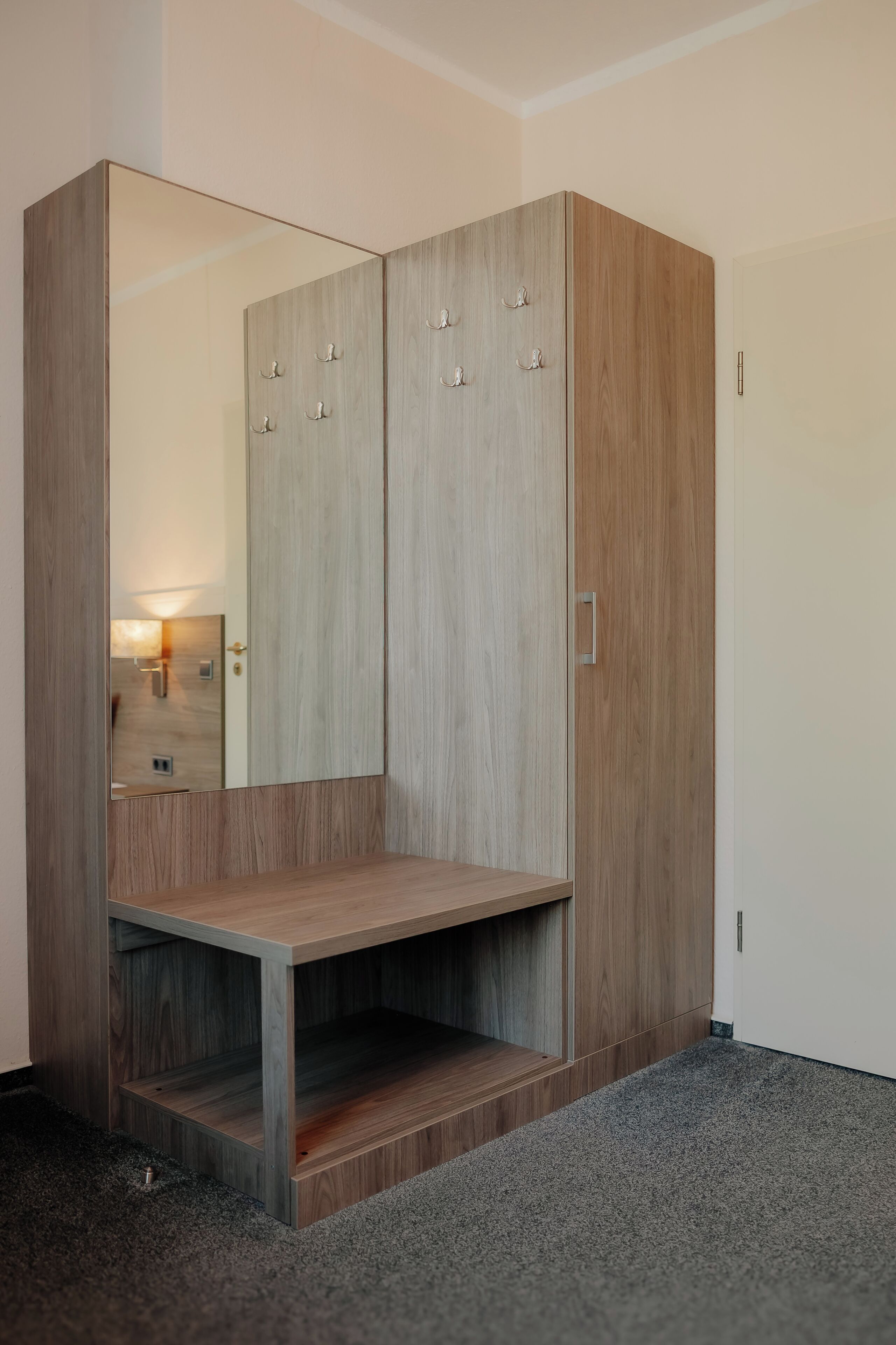 A wardrobe with a mirror, a wooden bench, and a door with a handle.