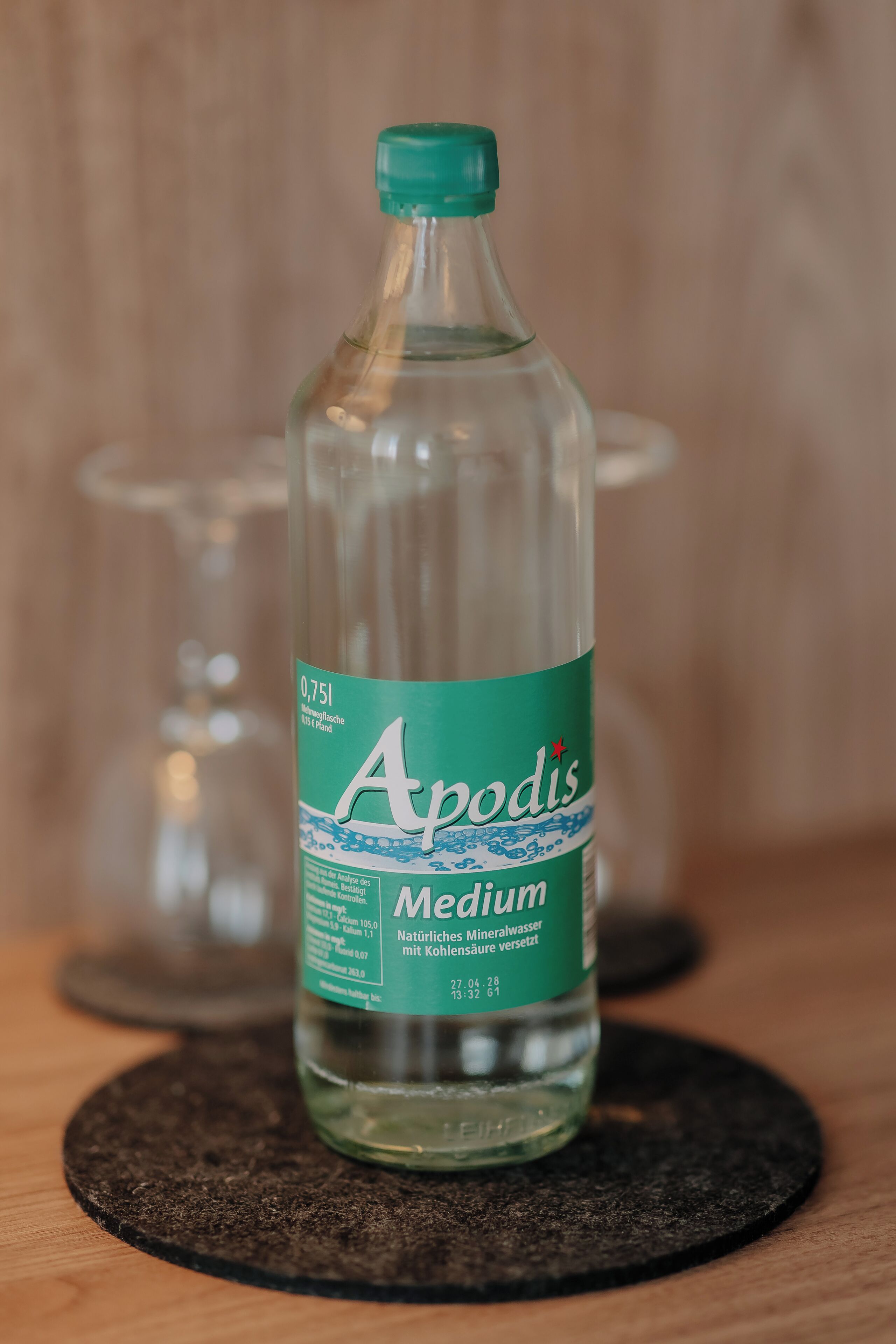 Una botella de vidrio transparente con agua mineral Apodis Medium sobre un posavasos.