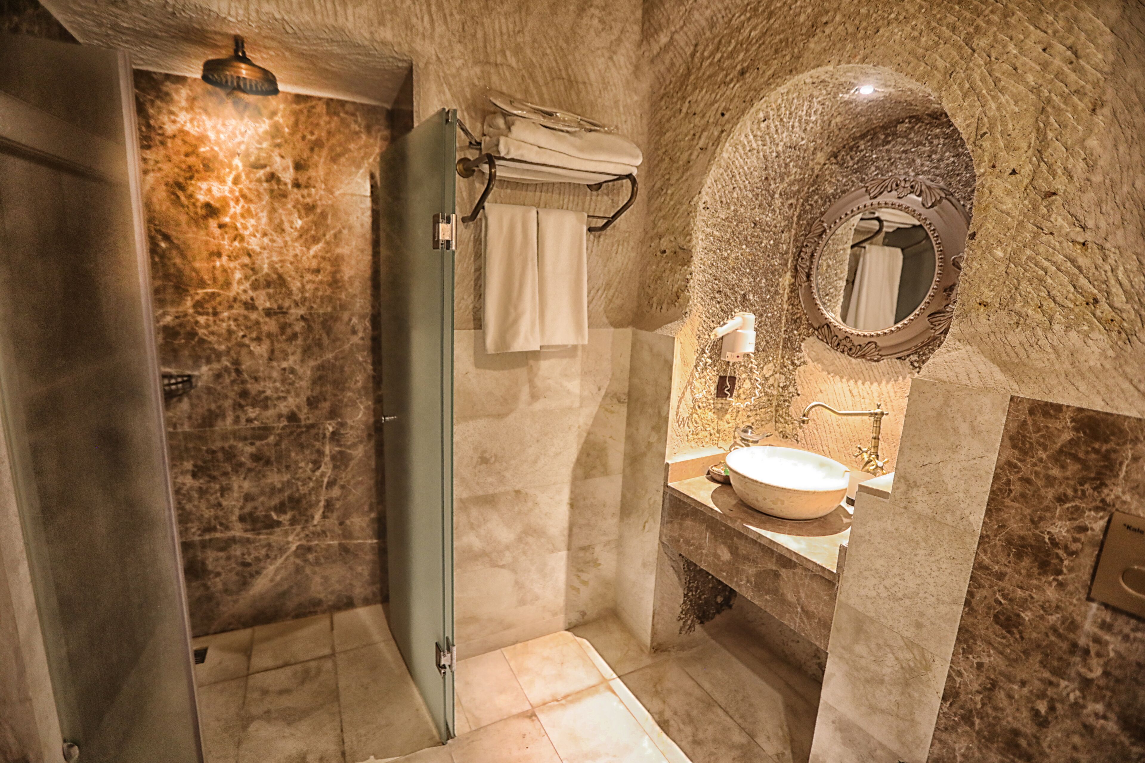A bathroom with a marble wall, a round mirror, a sink, and a shower.